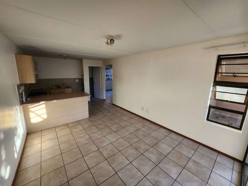 Open plan living and kitchen area featuring tiled flooring, breakfast bar, and louvered windows in a neutral, vacant space.