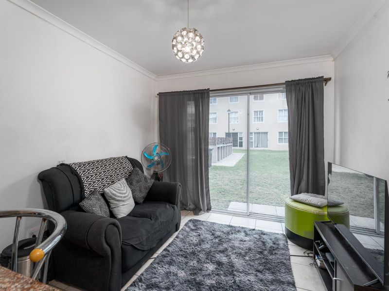 A compact living room featuring tiled flooring, a coved ceiling, and a sliding glass door providing access to the exterior garden area.