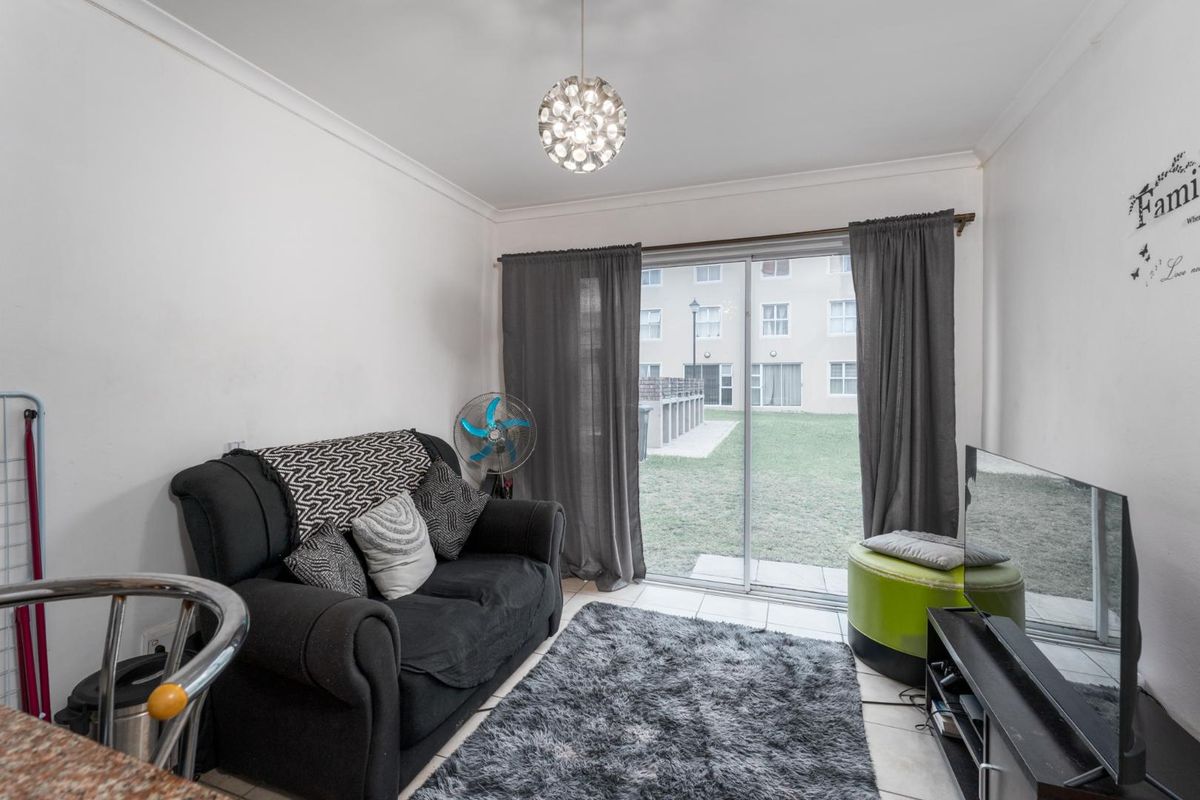 A compact living room featuring tiled flooring, a coved ceiling, and a sliding glass door providing access to the exterior garden area.