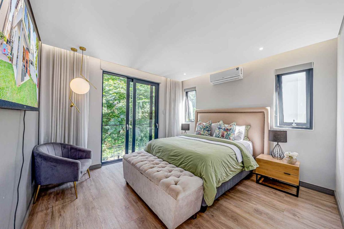 A modern, well-lit bedroom featuring laminate flooring, a split-system air conditioner, and large aluminium sliding doors that provide access to an outdoor view.