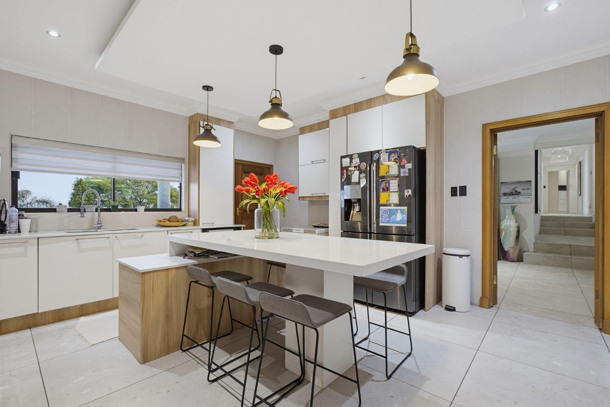 Modern kitchen featuring a central island with breakfast bar seating, sleek cabinetry, tiled flooring, and contemporary pendant lighting.