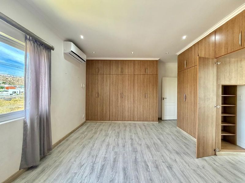 Spacious bedroom featuring extensive built-in wooden cabinetry, modern laminate flooring, recessed lighting, and a wall-mounted air conditioning unit.