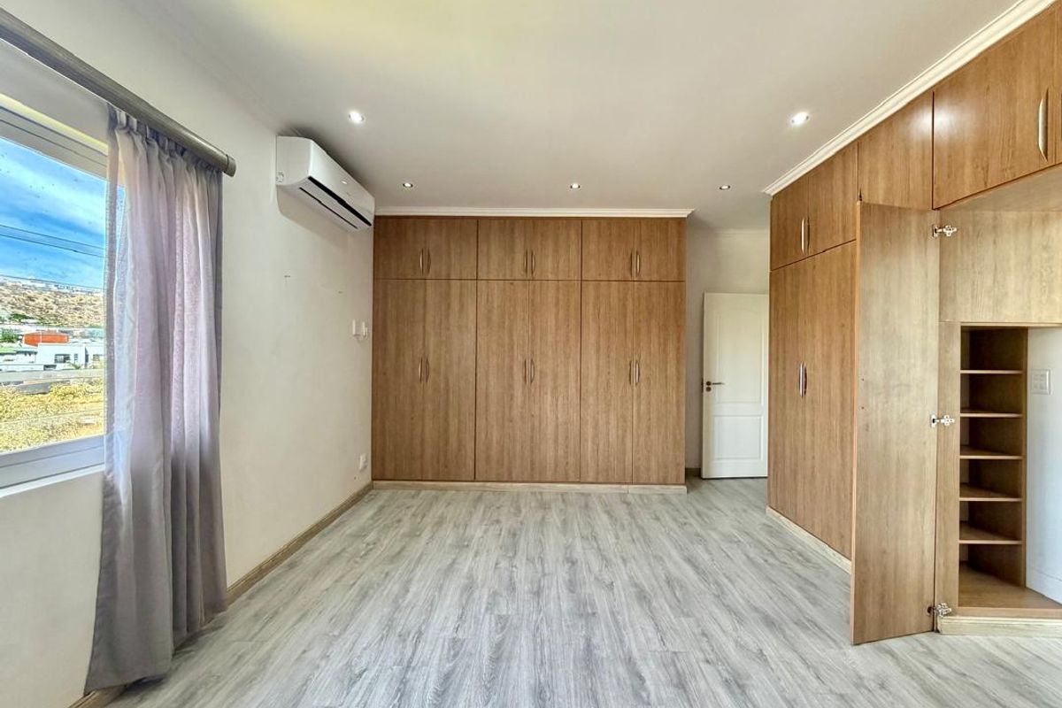 Spacious bedroom featuring extensive built-in wooden cabinetry, modern laminate flooring, recessed lighting, and a wall-mounted air conditioning unit.