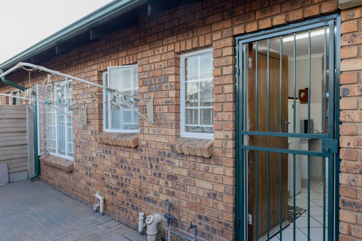 Rear exterior view of the townhouse featuring face-brick facade, security gate access, paved patio area, and wall-mounted washing line.