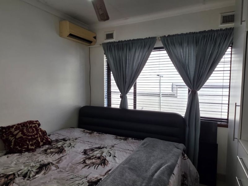 A compact bedroom featuring a built-in wardrobe, air conditioning unit, and venetian blinds, providing a functional and comfortable sleeping space.