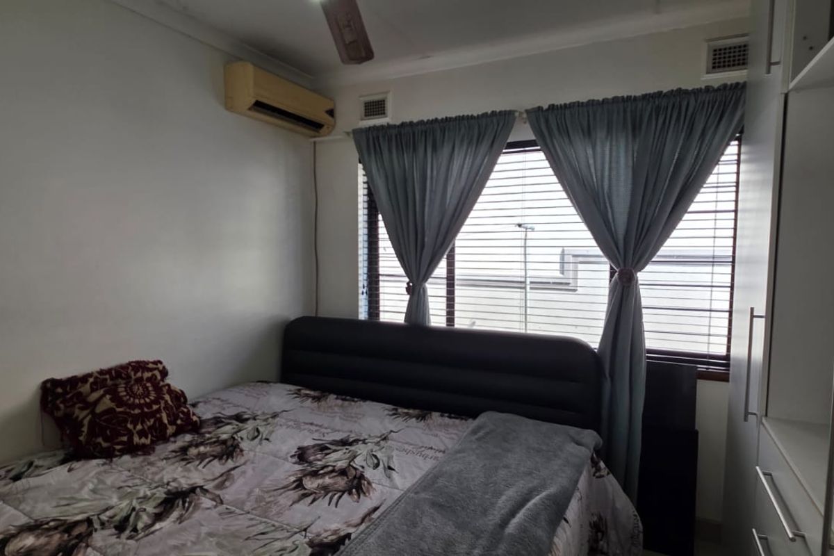 A compact bedroom featuring a built-in wardrobe, air conditioning unit, and venetian blinds, providing a functional and comfortable sleeping space.