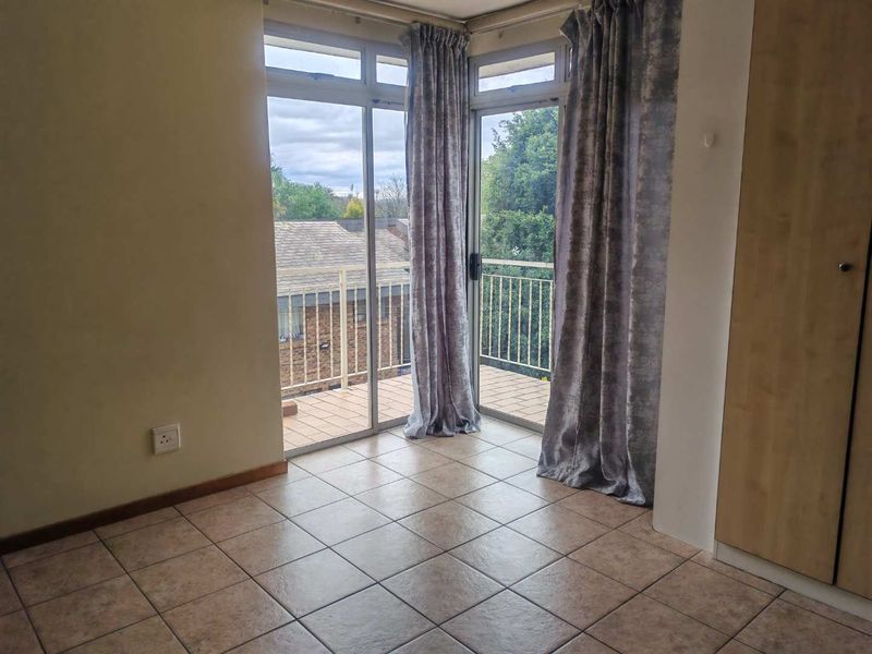 A bright bedroom featuring tiled flooring, a built-in cupboard, and sliding glass doors that open onto a private balcony.