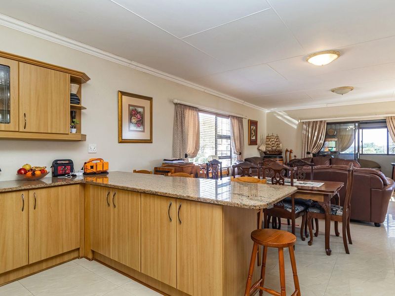 Open-plan living area featuring a kitchen with granite countertops and laminate cabinetry, flowing into a dining and lounge space with sliding door access.