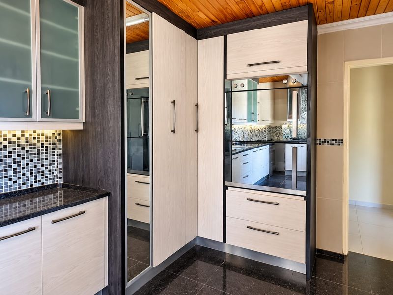 Modern kitchen featuring two-tone cabinetry, built-in oven, mosaic tile backsplash, granite countertops, and a warm timber ceiling finish.