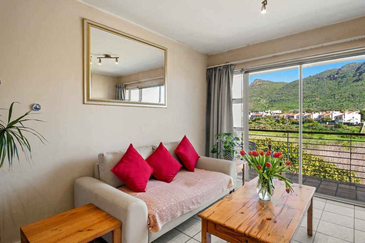 A bright living room featuring tiled flooring and large sliding glass doors that open onto a balcony with scenic mountain views.