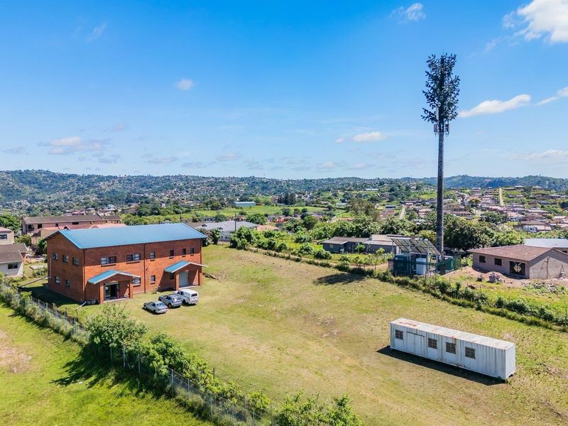 Aerial view of a residential vacant land plot featuring a brick building, a telecommunications tower, and surrounding neighborhood landscape.
