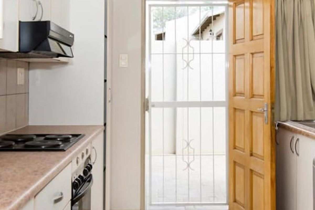 Functional kitchen featuring built-in cabinetry, electric hob, oven, and extractor fan, with direct access to an outdoor area through a secure timber door.