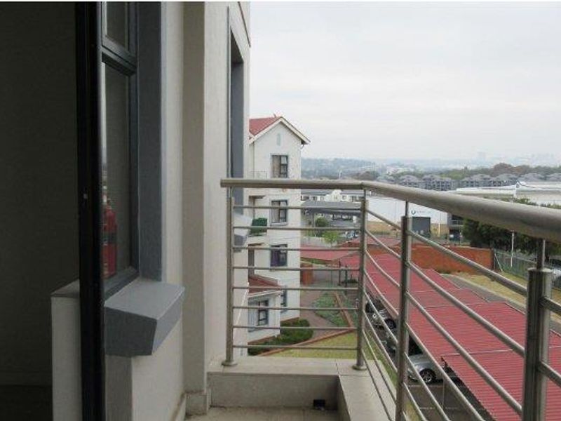 A private balcony featuring a stainless steel balustrade and tiled flooring, offering an elevated view of the surrounding apartment complex and parking area.