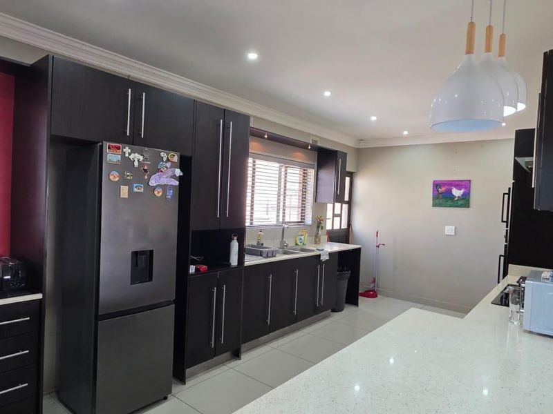 Modern kitchen featuring dark wood cabinetry, stone countertops, integrated appliances, and a breakfast bar, illuminated by recessed downlights and stylish pendant lighting.