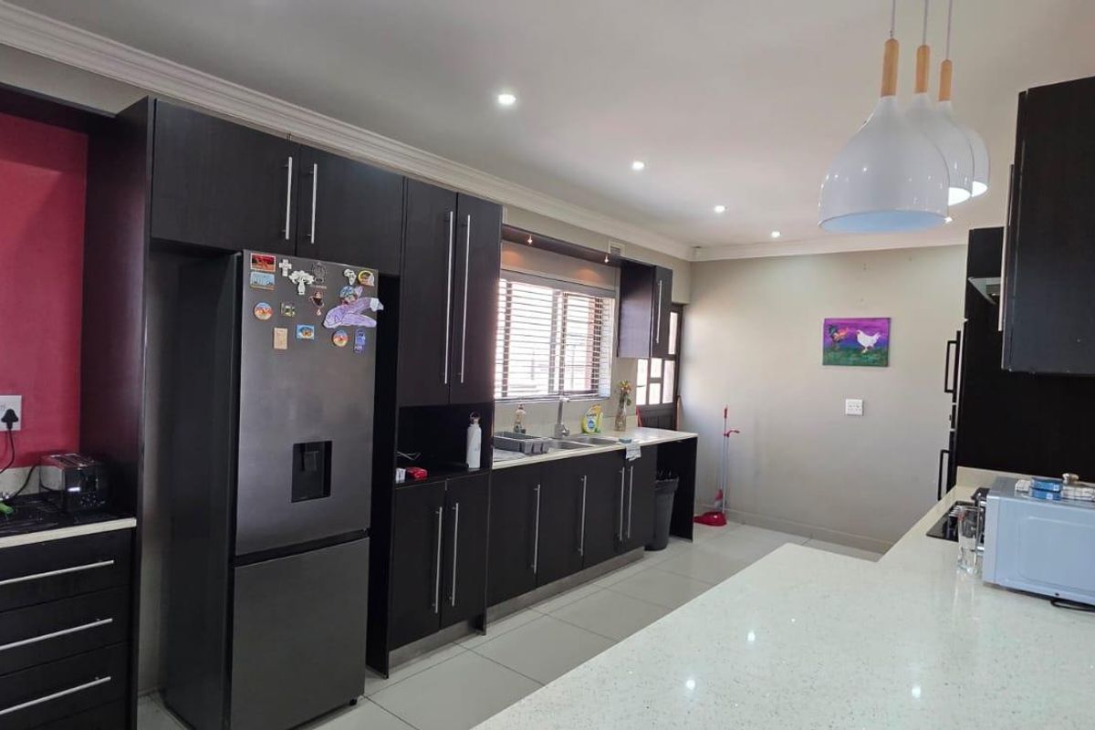 Modern kitchen featuring dark wood cabinetry, stone countertops, integrated appliances, and a breakfast bar, illuminated by recessed downlights and stylish pendant lighting.