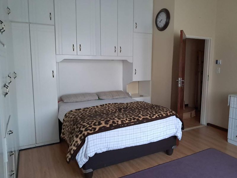 A bedroom featuring extensive white built-in cupboards and laminate flooring, providing ample storage space and a functional layout.