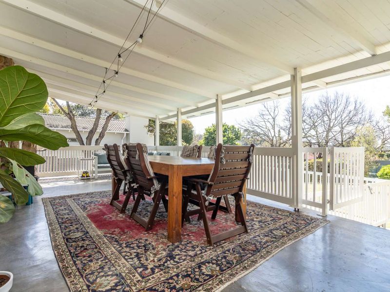 A spacious covered patio featuring a painted timber ceiling, concrete flooring, and a white timber balustrade, overlooking the garden area.
