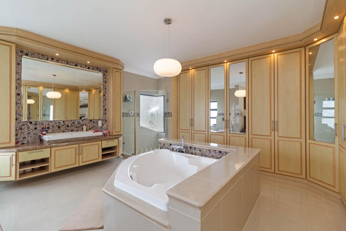 Spacious primary bathroom featuring a central built-in soaking tub, extensive light wood cabinetry, large vanity mirror, and a separate glass-enclosed shower.