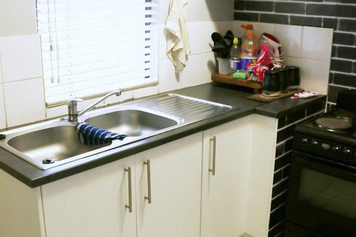 Compact kitchen featuring white cabinetry, black subway tile backsplash, stainless steel double sink, and an electric stove with ceramic tiled flooring.