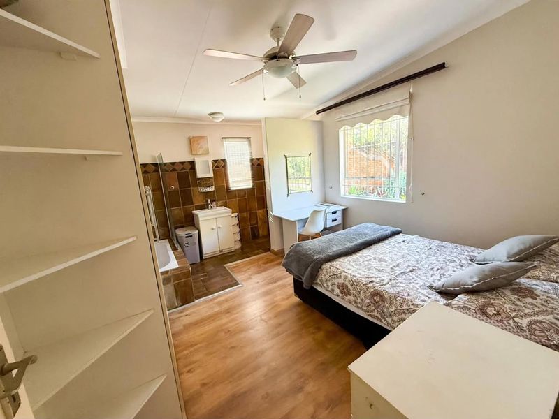 A bedroom featuring laminate flooring, a ceiling fan, and an integrated en-suite bathroom area with tiled finishes and built-in shelving.