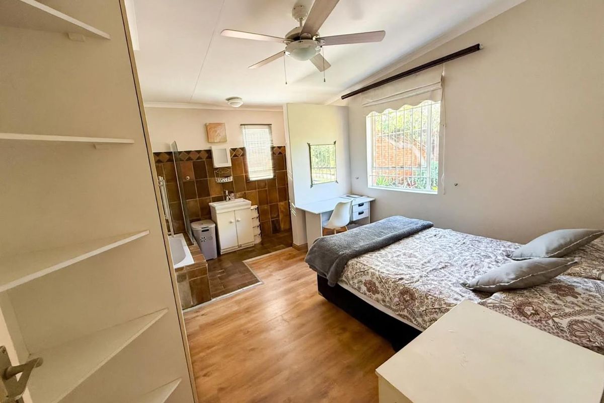 A bedroom featuring laminate flooring, a ceiling fan, and an integrated en-suite bathroom area with tiled finishes and built-in shelving.