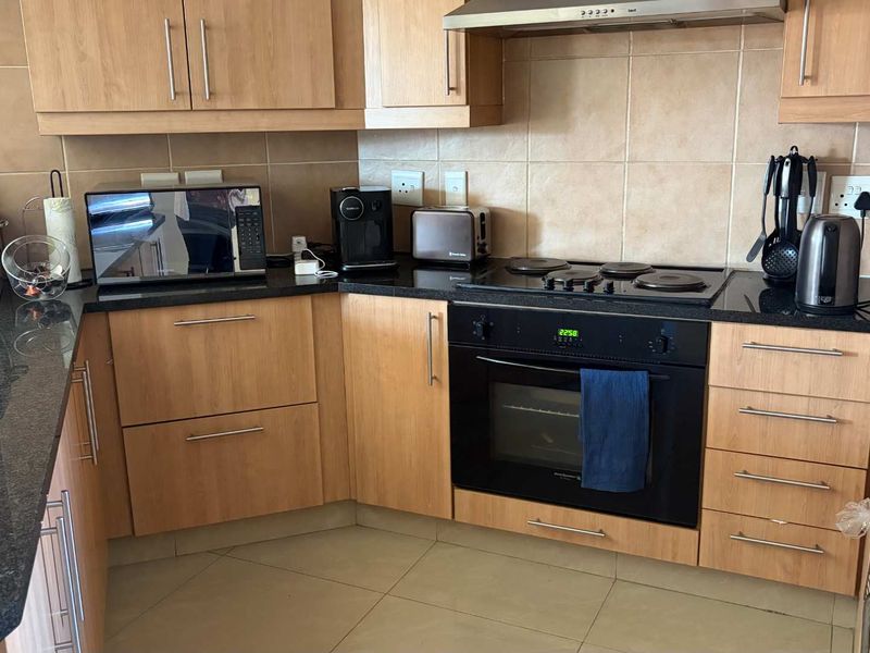A functional kitchen featuring light wood cabinetry, dark granite countertops, a built-in oven, electric hob, and a tiled backsplash.