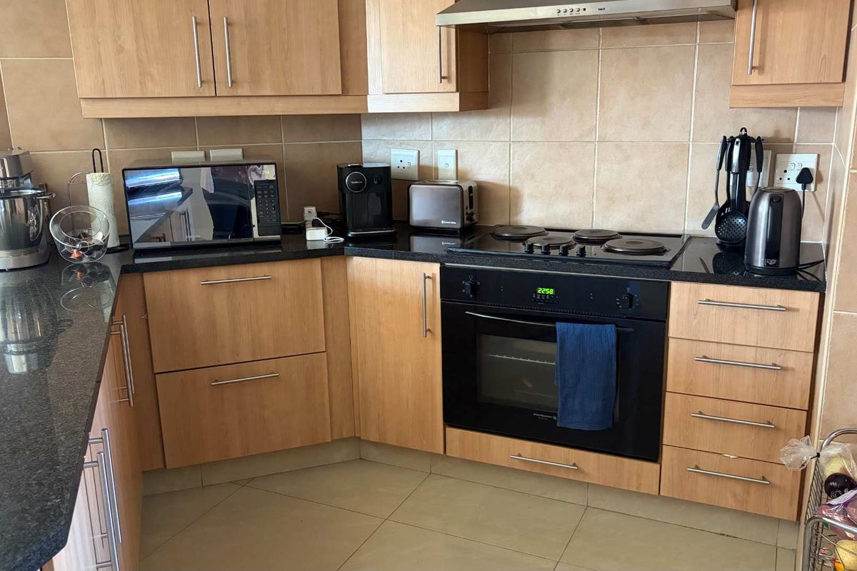 A functional kitchen featuring light wood cabinetry, dark granite countertops, a built-in oven, electric hob, and a tiled backsplash.