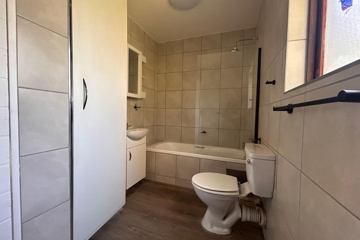 A functional bathroom featuring a bathtub with a glass shower screen, a wall-mounted basin, and a standard toilet with tiled walls.