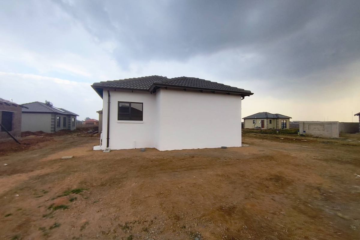 A view of the rear exterior elevation of a modern residential house featuring a tiled roof and white plastered walls in a developing estate.