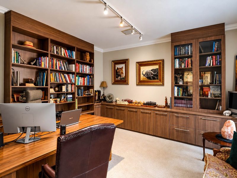 A well-appointed home office featuring extensive custom built-in wooden cabinetry, integrated bookshelves, and professional track lighting.