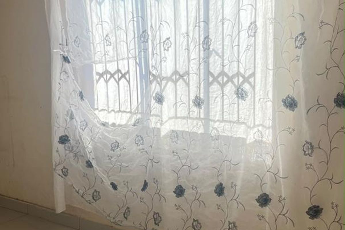 An empty bedroom featuring tiled flooring, security bars on the window, and patterned ceiling tiles in need of maintenance.