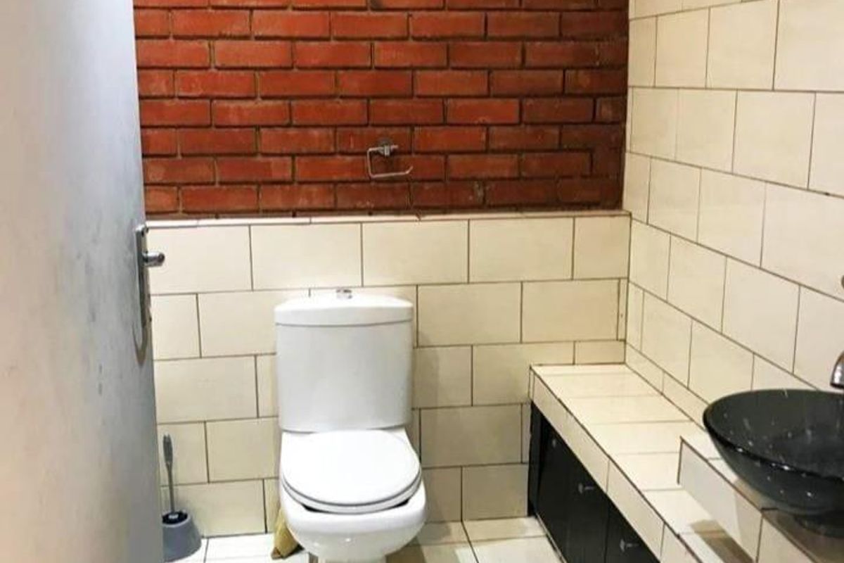 A compact bathroom featuring a white ceramic toilet, a black vessel sink set on a tiled vanity, and a distinctive exposed red brick feature wall.