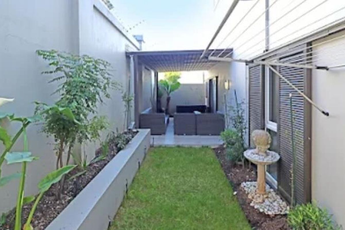 A narrow rear garden featuring a covered patio area, a raised garden bed, and a wall-mounted washing line along the side of the property.