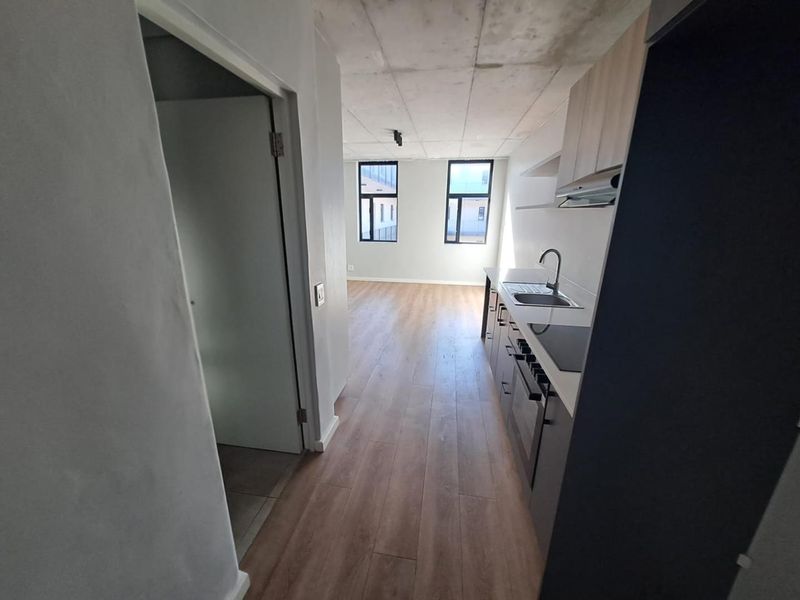 Modern open-plan apartment featuring an exposed concrete ceiling, laminate flooring, and a compact kitchen with built-in appliances and cabinetry.