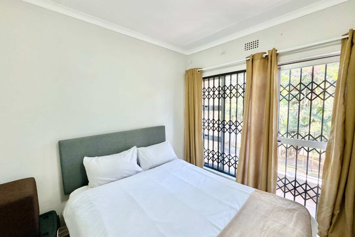 A bedroom featuring neutral walls, a sliding glass door with security gate, and access to an outdoor area.