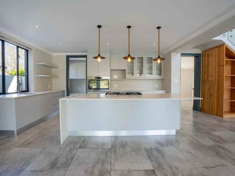 Modern kitchen featuring a central island with gas hob, stone countertops, sleek cabinetry, and integrated appliances, complemented by stylish pendant lighting and tiled flooring.