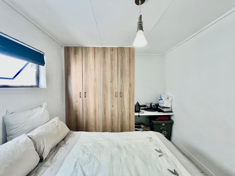 A functional bedroom featuring a wood-finish built-in wardrobe, a built-in desk area, and a pendant light fixture.