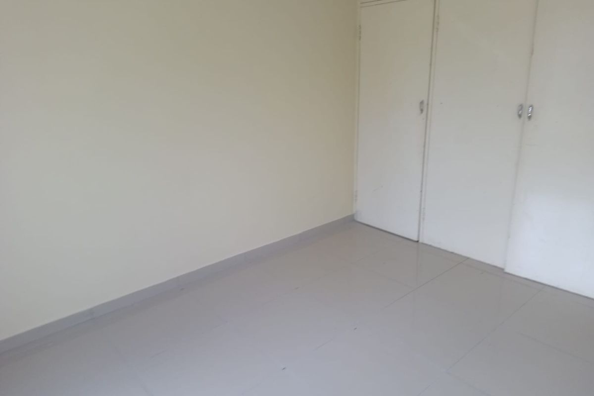 A vacant bedroom featuring neutral tiled flooring and built-in storage cupboards.