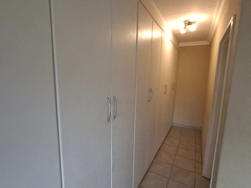 A functional hallway featuring extensive built-in storage cupboards and neutral tiled flooring, providing efficient circulation and storage space within the townhouse.
