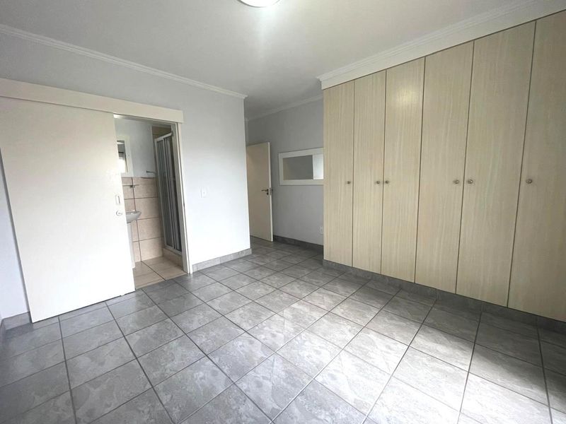 A spacious, empty bedroom featuring neutral tiled flooring, extensive built-in cupboards, and direct access to an en-suite bathroom.
