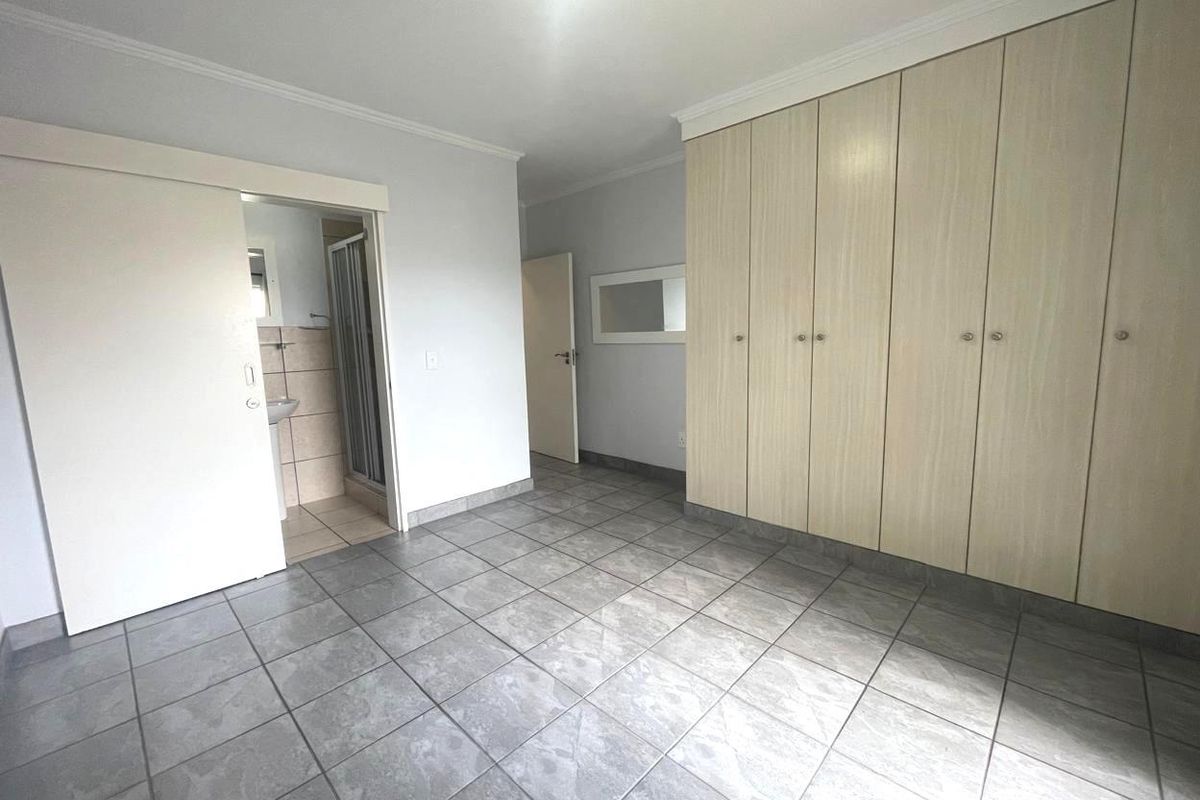 A spacious, empty bedroom featuring neutral tiled flooring, extensive built-in cupboards, and direct access to an en-suite bathroom.
