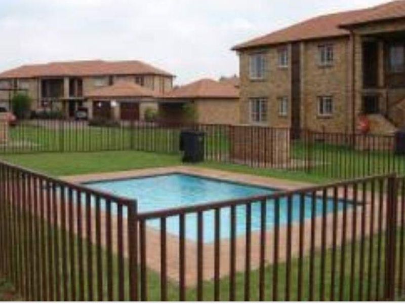 A communal swimming pool area within an apartment complex, featuring paved surrounds and secure metal perimeter fencing.