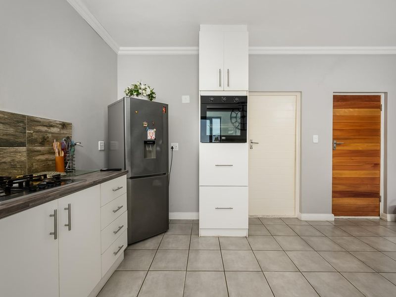 A modern kitchen featuring white cabinetry, a built-in oven, gas hob, laminate countertops, and neutral tiled flooring with a timber door.