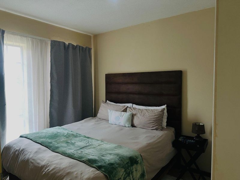 A standard bedroom featuring neutral wall tones and natural light access through a window with curtain tracks.