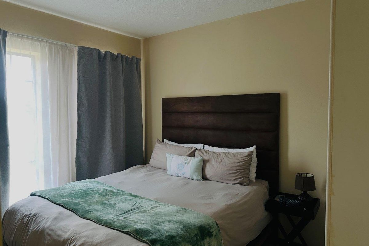 A standard bedroom featuring neutral wall tones and natural light access through a window with curtain tracks.