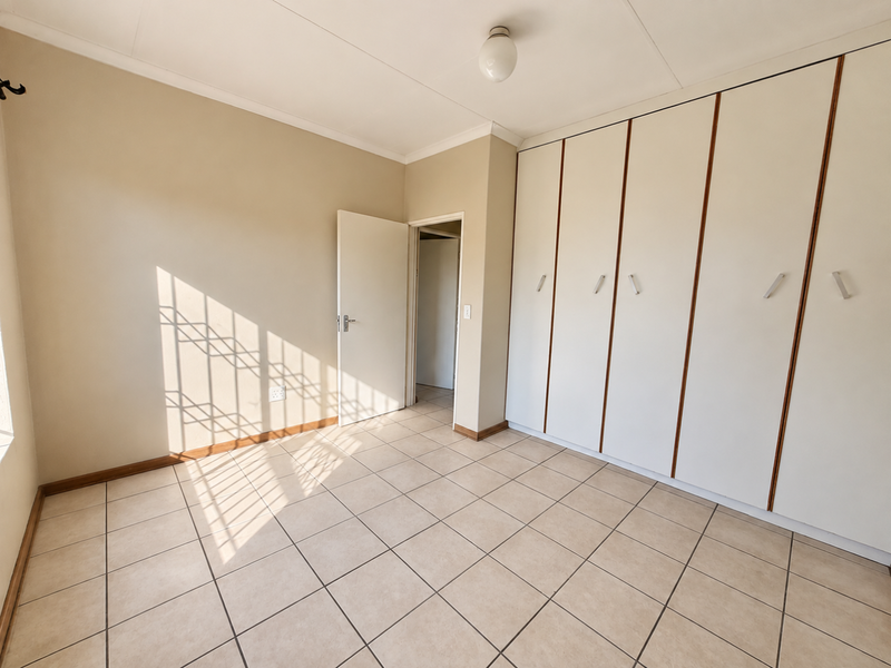 A bright, empty bedroom featuring neutral tiled flooring and extensive built-in cupboard storage, offering a clean and versatile space.