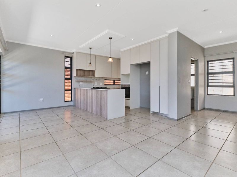Modern open-plan living and kitchen area featuring neutral cabinetry, built-in appliances, tiled flooring, and recessed lighting in a clean, contemporary space.