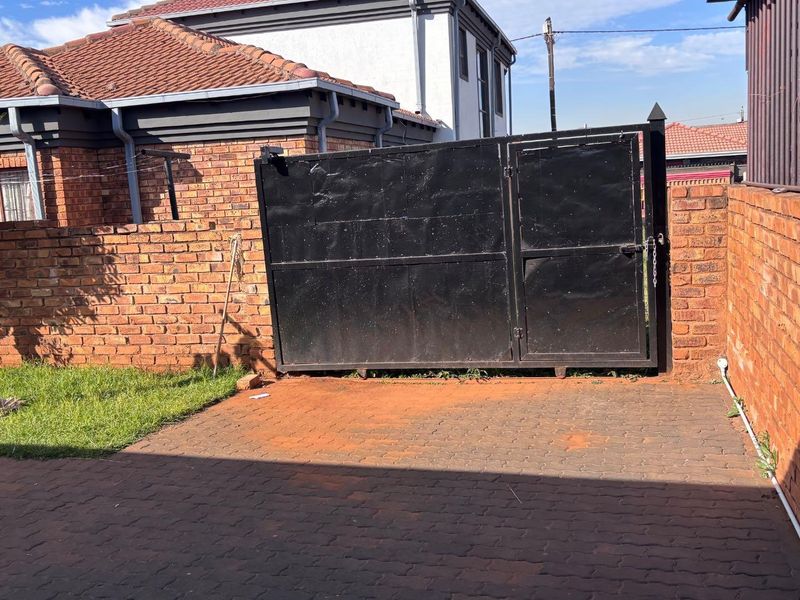 A private rear courtyard featuring a paved driveway, brick boundary walls, and a large black metal security gate.