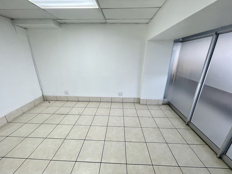 A vacant office space featuring ceramic floor tiles, a suspended ceiling with integrated lighting, and a frosted glass partition wall.