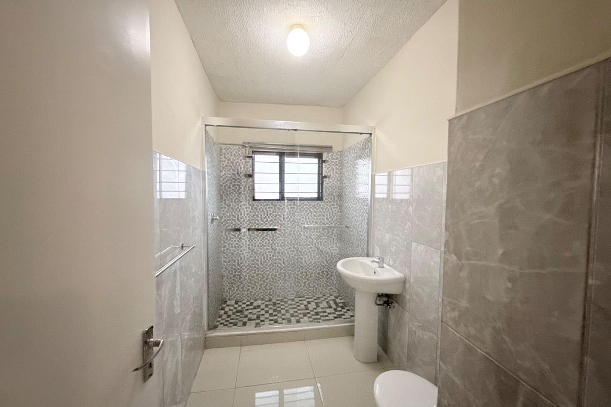 A modern bathroom featuring a glass-enclosed shower with mosaic tiling, a pedestal basin, and neutral wall and floor tiles.